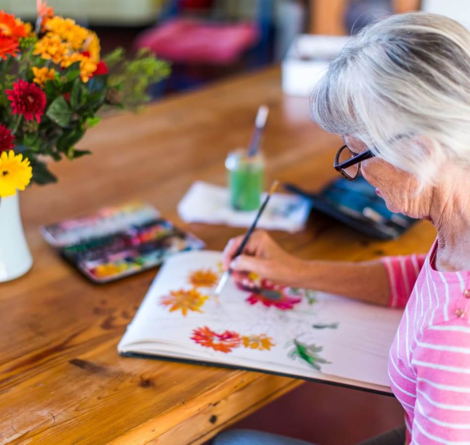 Senior painting colorful flowers during a hands-on creative activity at The Village of the Heights.