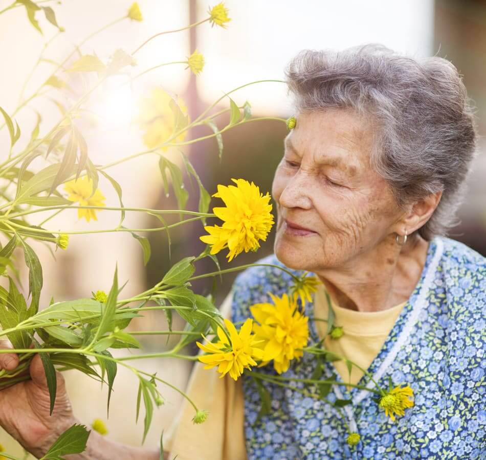 Elderly woman in a memory care program smiling sniffing flowers